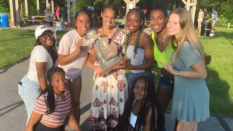 Schülerinnen der Huron High School halten im Freien gemeinsam einen Pokal und stehen vor Gebäuden und Bäumen.