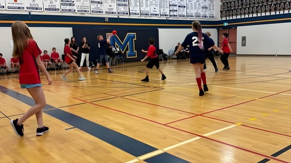 Schüler spielen Basketball auf dem Holzplatz mit dem großen M-Logo beim Huron-Perth Catholic District School Board.