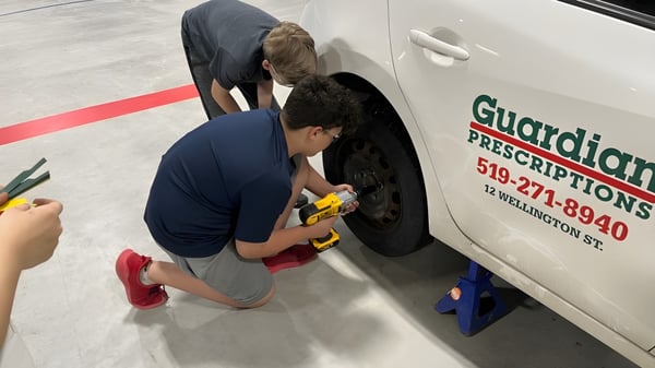 Eine Person kniet am Boden neben einem Van der Huron-Perth Catholic District School Board und inspiziert das Fahrzeug.