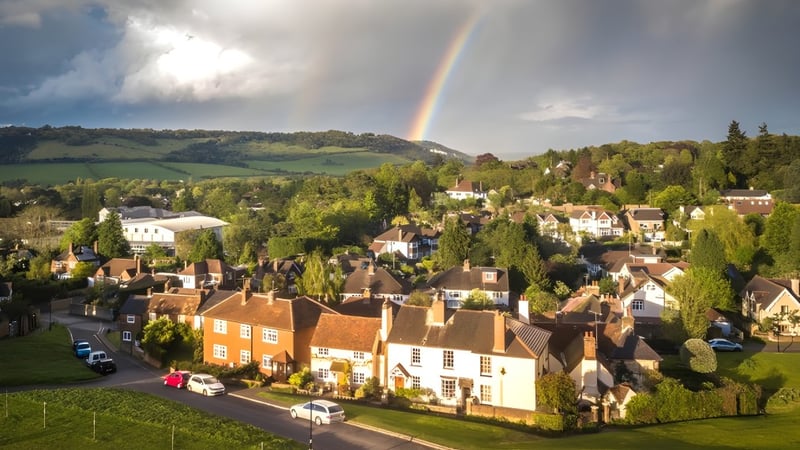 Eine malerische Landschaft mit einem Regenbogen über einem Dorf auf dem Gelände der Hurtwood House.