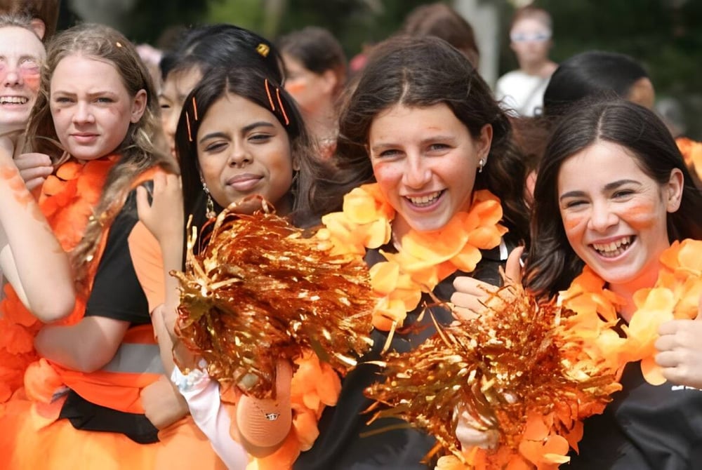 Schüler der Hutt Valley High School sind in orange und gelb gekleidet und zeigen beim Cheerleading im Grünen ihre Pompons.