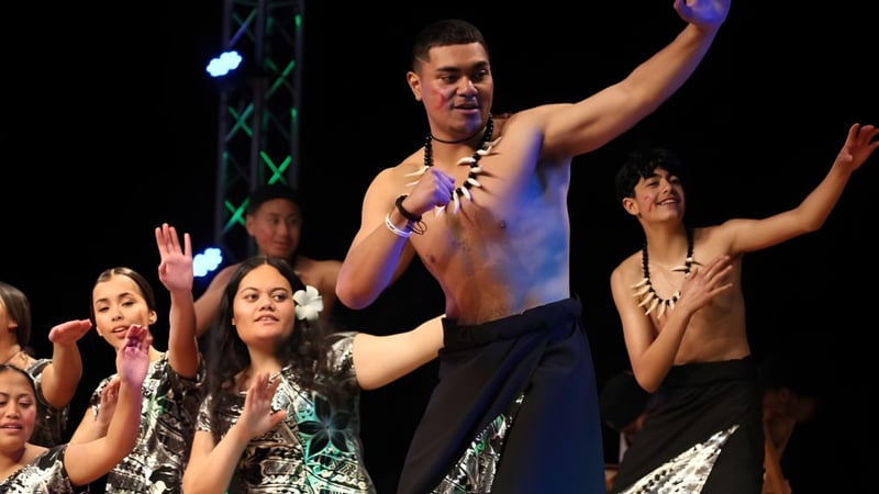 Ein shirtless männlicher Performer steht auf der Bühne vor einer Gruppe weiblicher Schülerinnen der Hutt Valley High School mit erhobenen Händen.