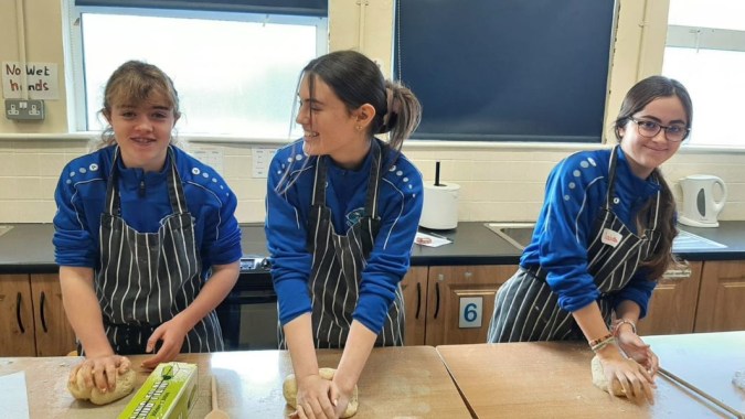 Drei Schüler in blauen Schürzen stehen hinter einem Tresen in der Küche des Iascaigh College.