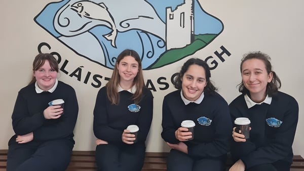 Vier Schülerinnen und Schüler in Schuluniformen stehen vor einem Wandgemälde mit Burg und Landschaft auf dem Campus des Iascaigh College.