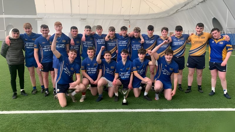 Eine Gruppe von jungen Athletinnen und Athleten des Iascaigh College posiert auf einem Sportfeld vor einer großen Sporthalle.