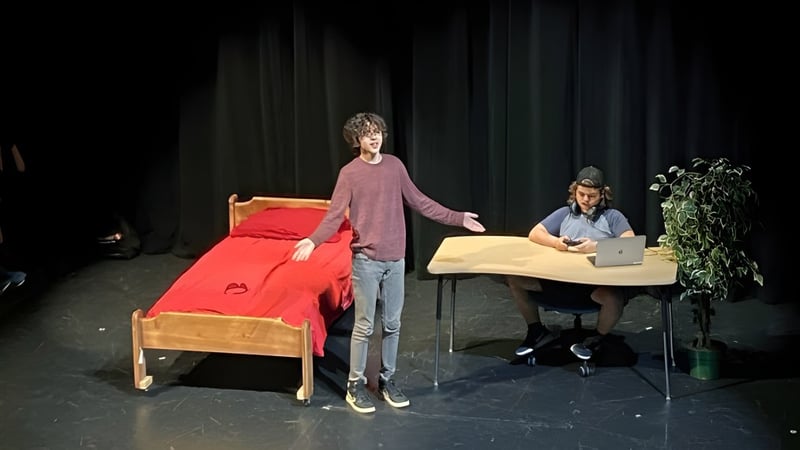 Eine Schülerin im pinken Shirt steht auf der Bühne der Imagine High Integrated Arts and Technology Secondary School mit rotem Sofa und Person am Tisch im Hintergrund.