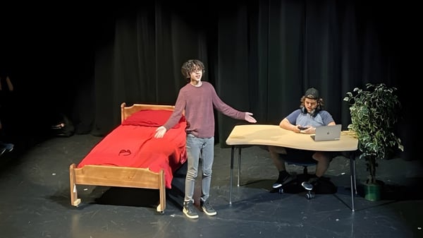 Eine Schülerin im pinken Shirt steht auf der Bühne der Imagine High Integrated Arts and Technology Secondary School mit rotem Sofa und Person am Tisch im Hintergrund.