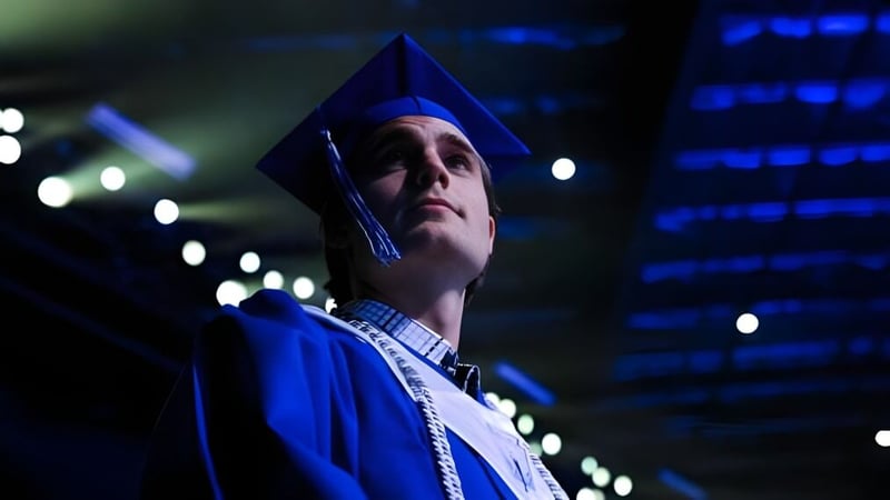 Eine Person in blauer Abschlussrobe und Mütze steht im gedämmten Licht auf dem Campus der IMG Academy.