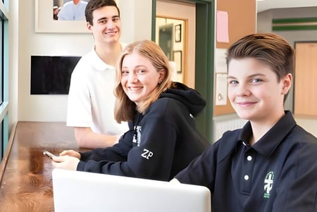 Drei Schülerinnen und Schüler der Immaculata Regional School stehen zusammen lächelnd in einer Lobby.