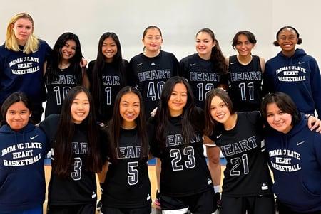 Eine Gruppe von Schülerinnen der Immaculate Heart High School posiert in ihren Basketballuniformen in einer Sporthalle.