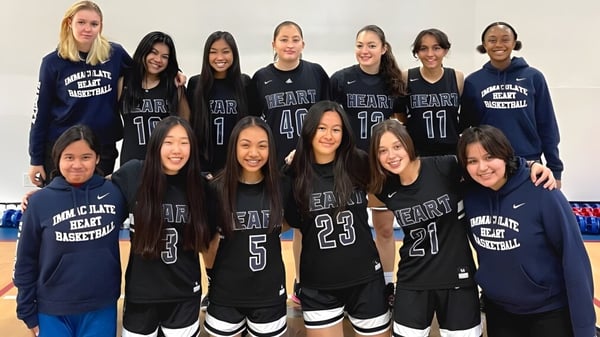 Eine Gruppe Schülerinnen der Immaculate Heart Central School posiert in einheitlichen Basketball-Trikots vor weißem Hintergrund.