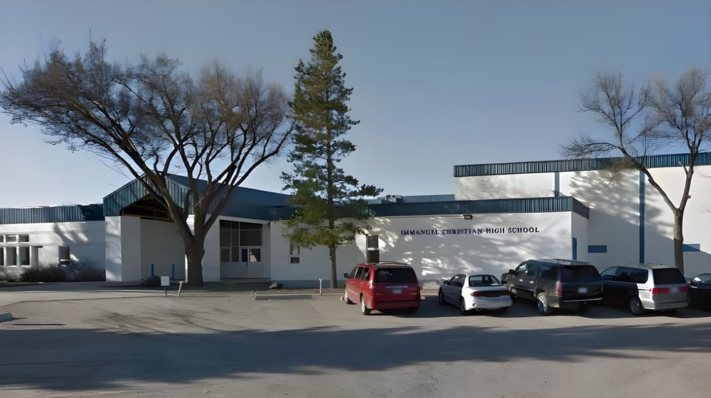 Das Gebäude der Immanuel Christian Secondary School steht hinter Bäumen und geparkten Autos.