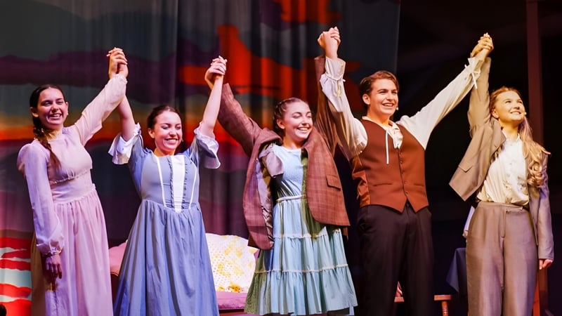 Fünf Frauen stehen auf der Bühne der Indian River Charter High School und heben ihre Arme in einer feierlichen Geste.