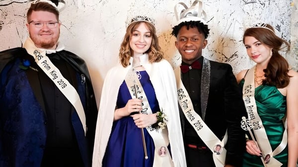 Vier Personen in formeller Kleidung posieren vor einer mit Graffiti bedeckten Wand auf dem Gelände der Indian River Charter High School.