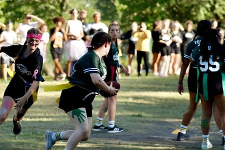 Eine Gruppe von Schülern der Indian River Charter High School versammelt sich auf einem Sportfeld mit umliegenden Bäumen.