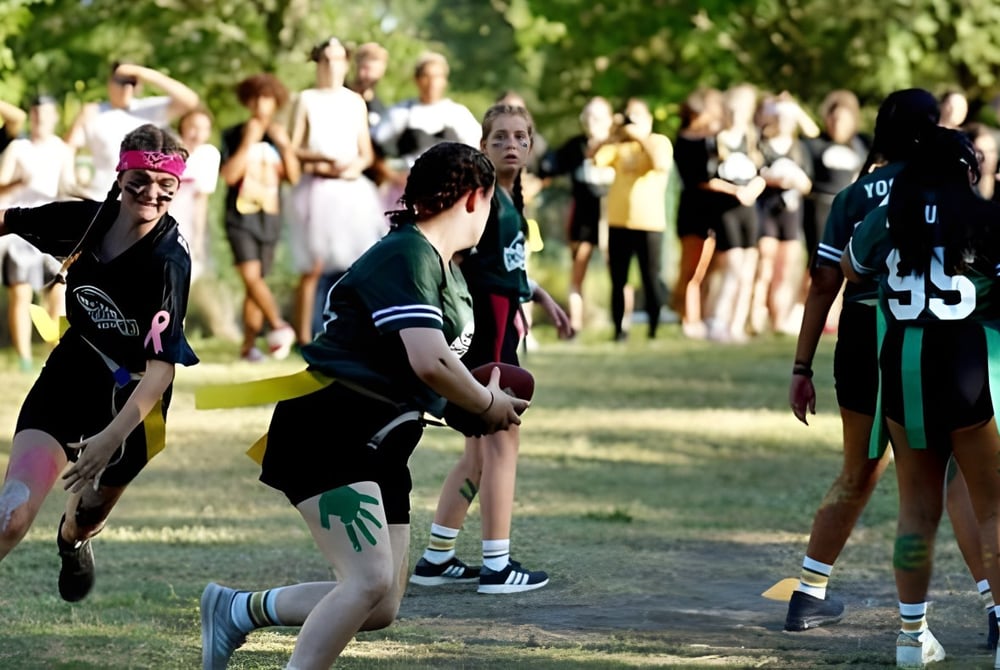 Eine Gruppe von Schülern der Indian River Charter High School versammelt sich auf einem Sportfeld mit umliegenden Bäumen.