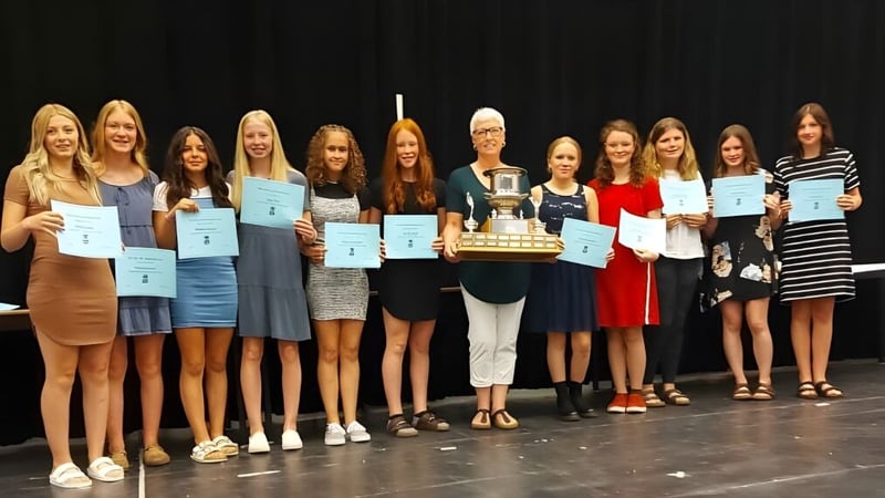 Schülerinnen der Indian River High stehen gemeinsam auf der Bühne und halten Urkunden und einen Pokal.