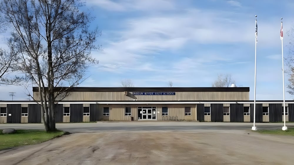 Das große braune Schulgebäude der Indian River High ist von Bäumen und einer Wiese umgeben.