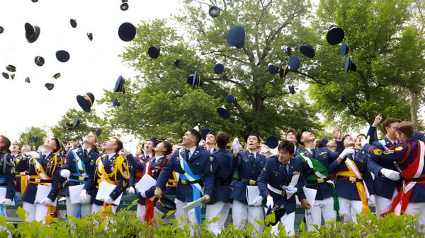 Schüler der Indiana Private Highschool tragen traditionelle japanische Uniformen und werfen ihre Hüte auf einer Wiese in die Luft.
