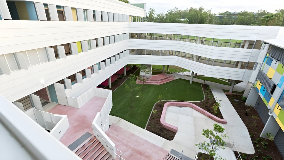 Das moderne mehrstöckige Gebäude der Indooroopilly State High School mit einem Innenhof und pinken Wegen ist zu sehen.