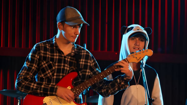 Zwei Schüler der Inglewood High School treten auf einer Bühne mit rotem Vorhang auf, einer spielt Gitarre.