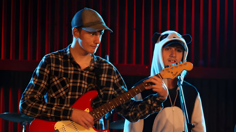 Zwei Schüler der Inglewood High School treten auf einer Bühne mit rotem Vorhang auf, einer spielt Gitarre.