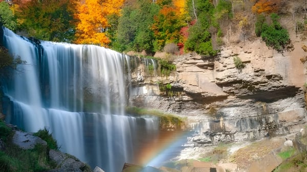 Ein Wasserfall fließt über eine Felsklippe mit herbstlichem Laub im Hintergrund auf dem Campus der Innisdale Secondary School.