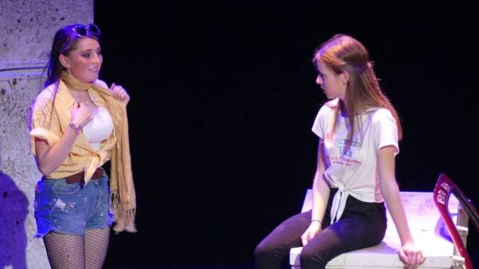 Zwei Schülerinnen stehen auf der Bühne des Institut Saint-Dominique vor dunklem Hintergrund mit lila Beleuchtung.