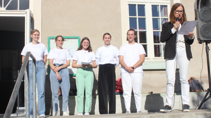 Eine Gruppe von Menschen steht vor dem Gebäude der Institution Mongazon, während eine Frau in ein Mikrofon spricht.