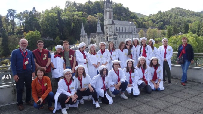 Schüler der Institution Mongazon stehen in weißen Roben vor einer großen kirchenähnlichen Fassade mit Bergen im Hintergrund.