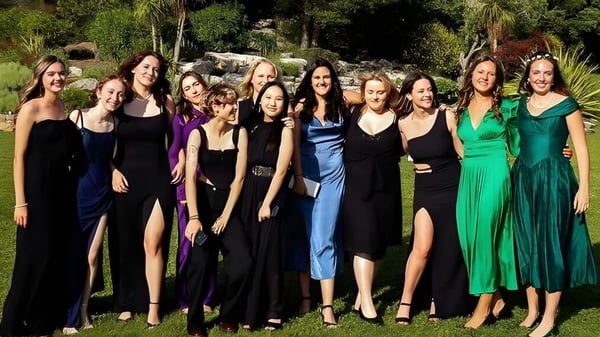 Eine Gruppe Schülerinnen der International Bilingual School of Provence steht in formellen Abendkleidern in einem grünen, natürlichen Umfeld.