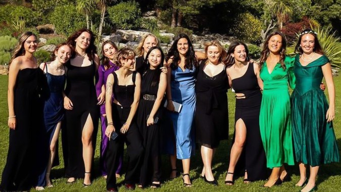 Eine Gruppe junger Frauen der International Bilingual School of Provence posiert in formeller Kleidung in einer natürlichen Umgebung mit Palmen.