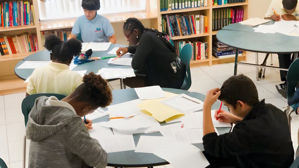 Eine Gruppe von Schülern der International School of Broward lernt gemeinsam in der Bibliothek umgeben von Bücherregalen.