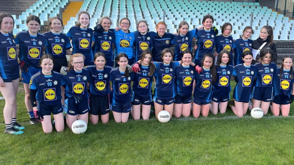 Eine Gruppe junger Fußballspielerinnen posiert gemeinsam auf dem Sportplatz des Inver College vor einer stadionähnlichen Struktur.