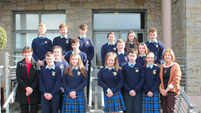 Eine Gruppe Schülerinnen und Schüler in Schuluniformen steht zusammen mit Erwachsenen vor einem steinernen Gebäude auf dem Campus des Inver College.