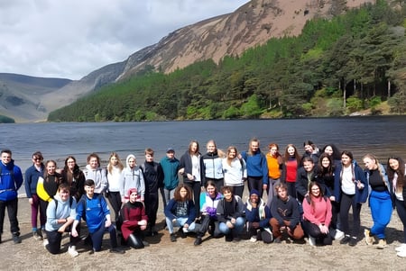 Eine Gruppe Schülerinnen und Schüler des Inver College versammelt sich an einem Strand vor einer bergigen Landschaft mit See im Hintergrund.