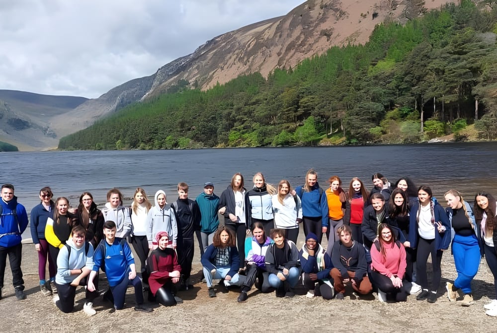 Eine Gruppe Schülerinnen und Schüler des Inver College versammelt sich an einem Strand vor einer bergigen Landschaft mit See im Hintergrund.