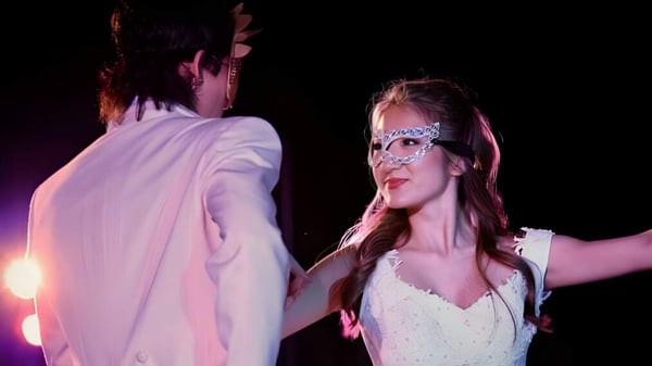 Eine Frau trägt ein weißes Kleid und eine Maske bei einer Veranstaltung der Iolani School mit bunter Hintergrundbeleuchtung.