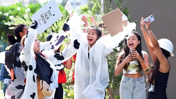 Eine Gruppe von Schülerinnen der Iolani School hält draußen Schilder hoch und jubelt vor grüner Kulisse.