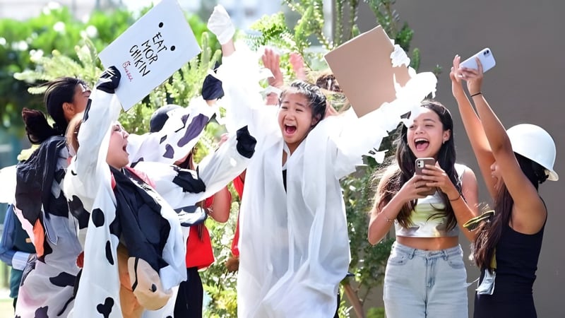 Eine Gruppe von Schülerinnen der Iolani School hält draußen Schilder hoch und jubelt vor grüner Kulisse.