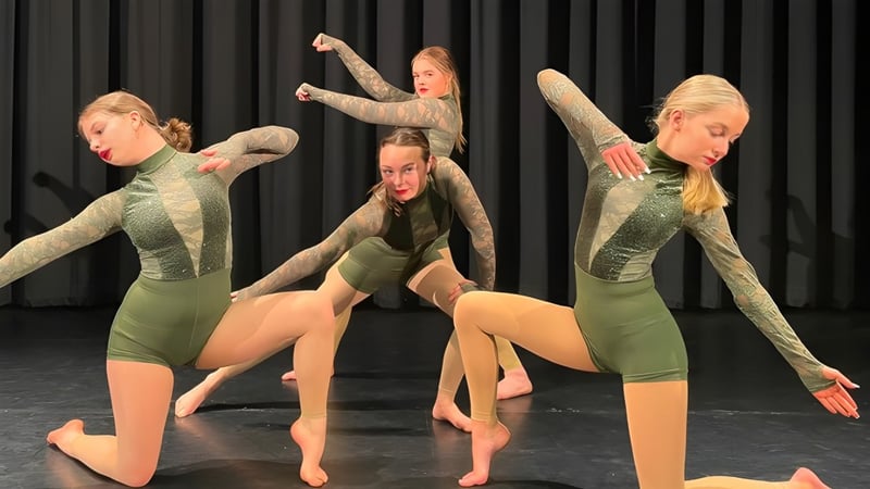 Schülerinnen der Ipswich High School führen eine synchronisierte Tanzdarbietung auf einer Bühne mit schwarzem Hintergrund auf.