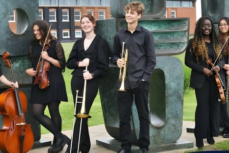 Eine Gruppe Musiker der Ipswich School steht mit verschiedenen Instrumenten vor einem Backsteingebäude.