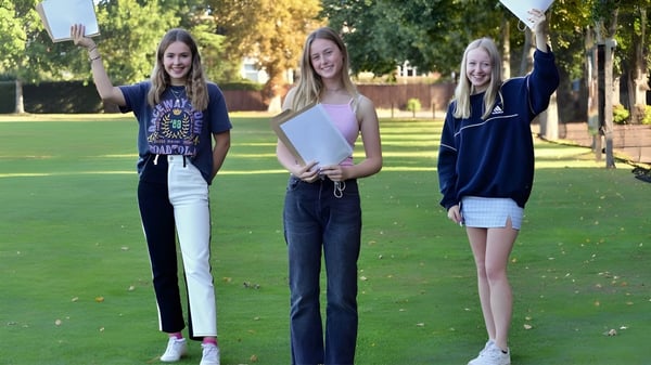 Drei Schülerinnen der Ipswich School stehen in einem Park auf einer Wiese und lächeln in die Kamera.
