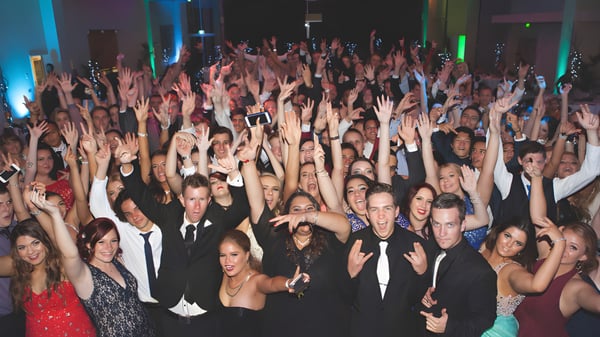 Eine große Gruppe von Schülerinnen und Schülern der Ipswich State High School hebt in einem bunt beleuchteten Veranstaltungsraum die Hände.