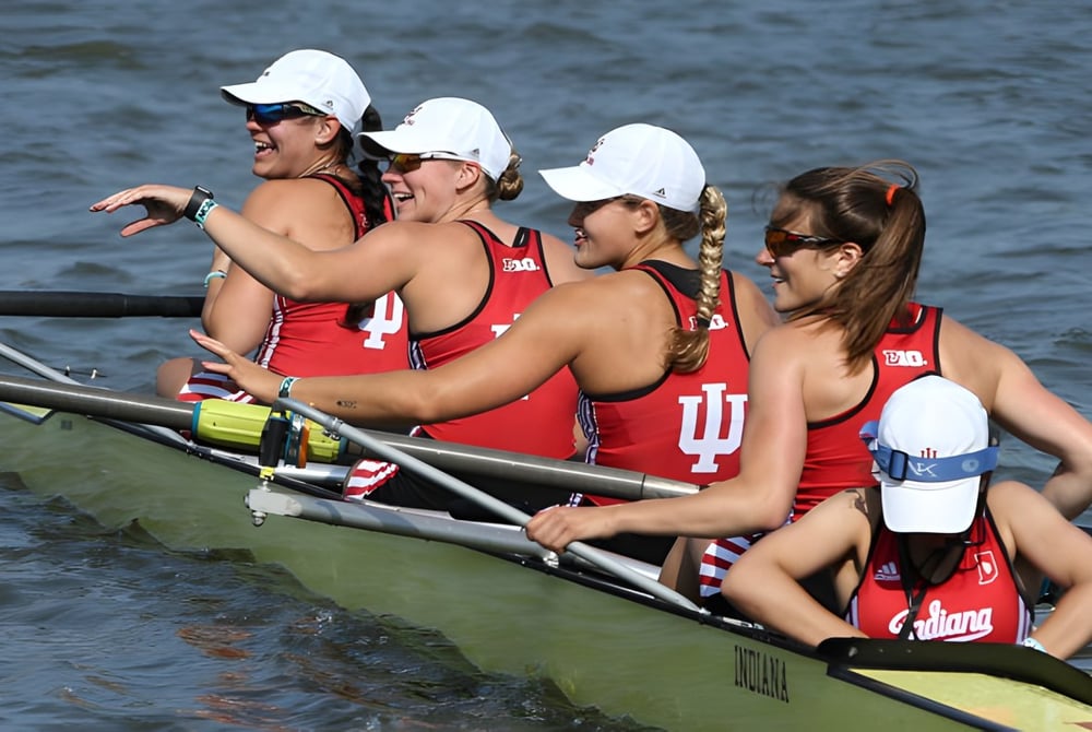 Schülerinnen der Ipswich State High School sitzen in roten Uniformen mit weißen Mützen in einem kleinen Boot auf dem Wasser.