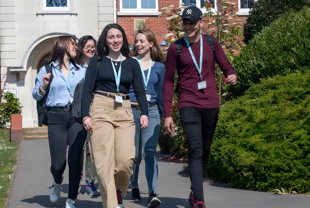 Schülerinnen und Schüler gehen gemeinsam auf einem Campusweg des Itchen Sixth Form College entlang, umgeben von Backsteingebäuden und Grünflächen.