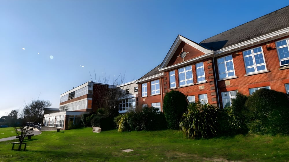 Das mehrstöckige Backsteingebäude des Itchen Sixth Form College mit großer Fensterfront vor einer Rasenfläche und Bäumen ist unter klarem Himmel zu sehen.