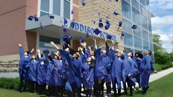 Eine Gruppe von Absolventen der J. Addison School feiert vor einem Backsteingebäude ihre akademischen Leistungen.