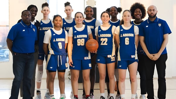 Eine Gruppe von Schülerinnen und Schülern der J. Addison School steht in blauen und weißen Basketballtrikots in einer Sporthalle.