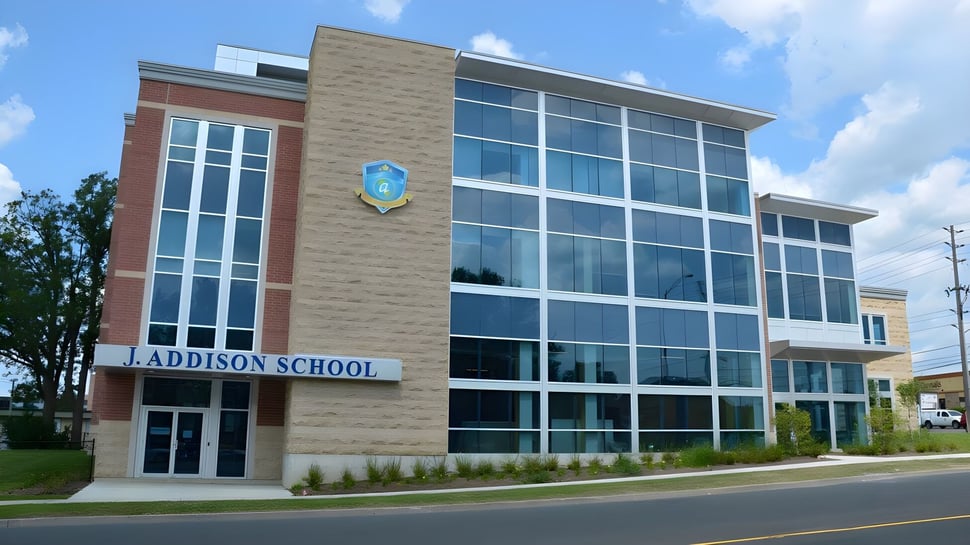 Das moderne Schulgebäude der J. Addison School mit großen Glasfenstern steht in einer parkähnlichen Umgebung.